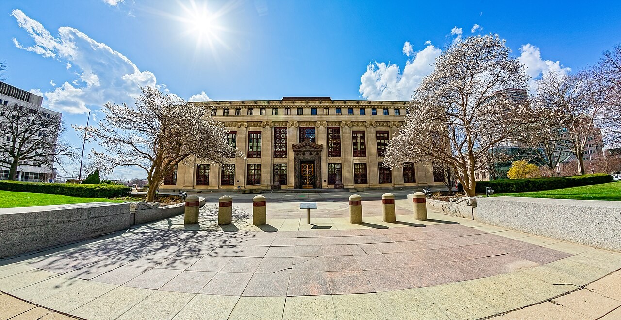 Exterior view of the neoclassical limestone facade of Columbus City Hall framed by trees and stone bollards on Portman Plaza.