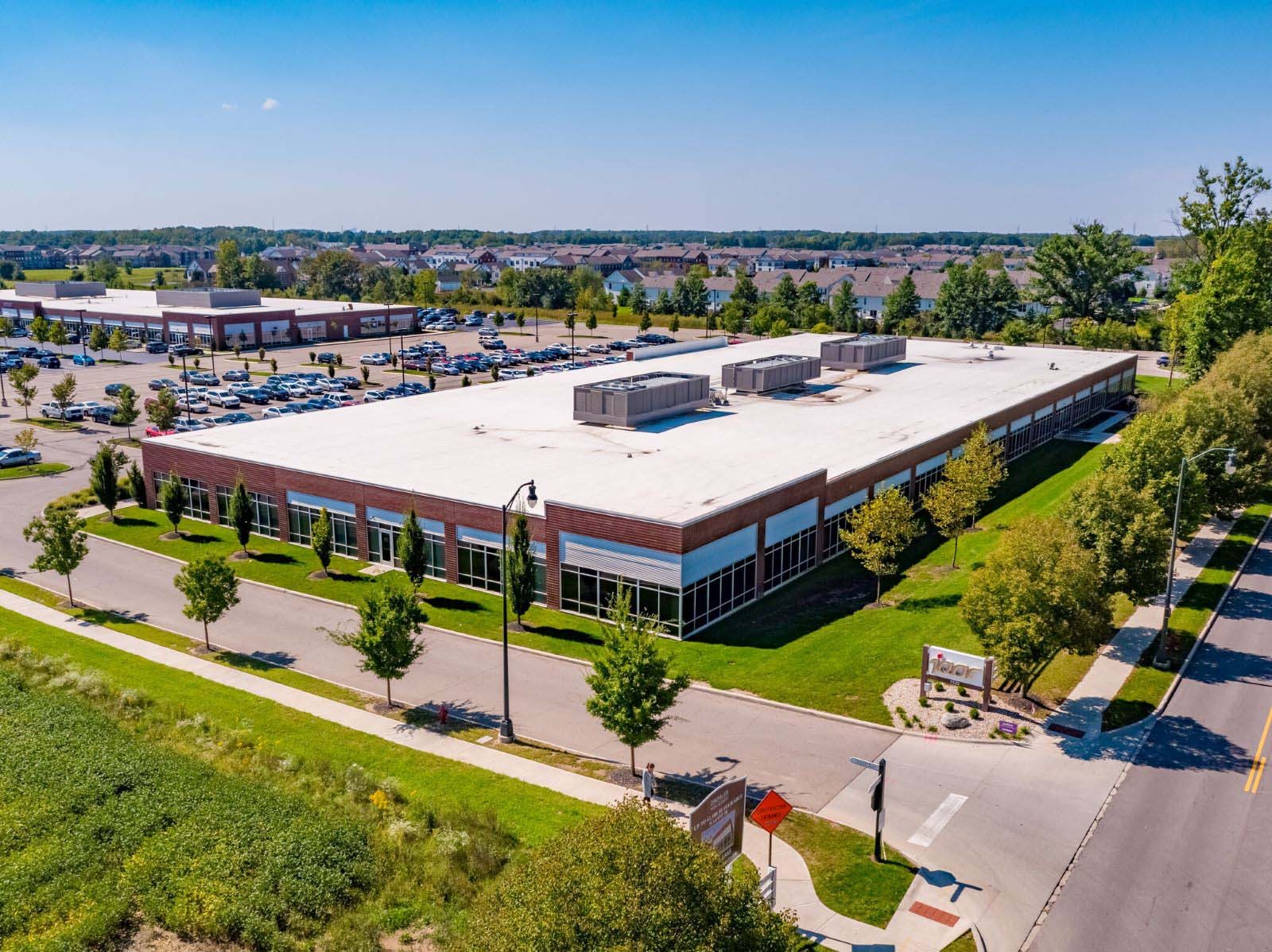 High-angle aerial photograph of the single-story brick school building and surrounding parking lot at 7525 W Campus Road in New Albany, Ohio.