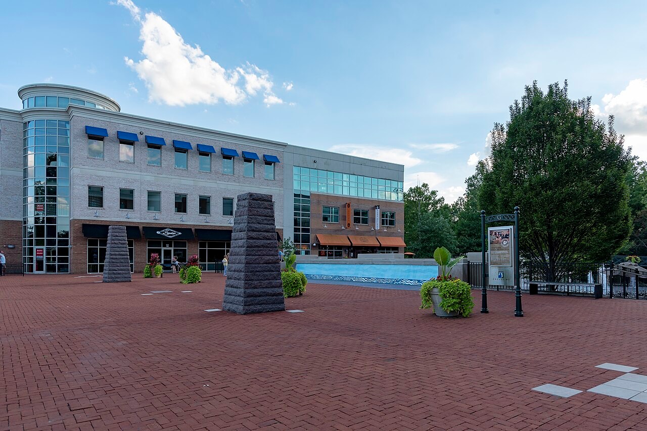 Red brick pedestrian plaza at Creekside Gahanna flanked by multi-story commercial buildings, stone monuments, and an information kiosk.