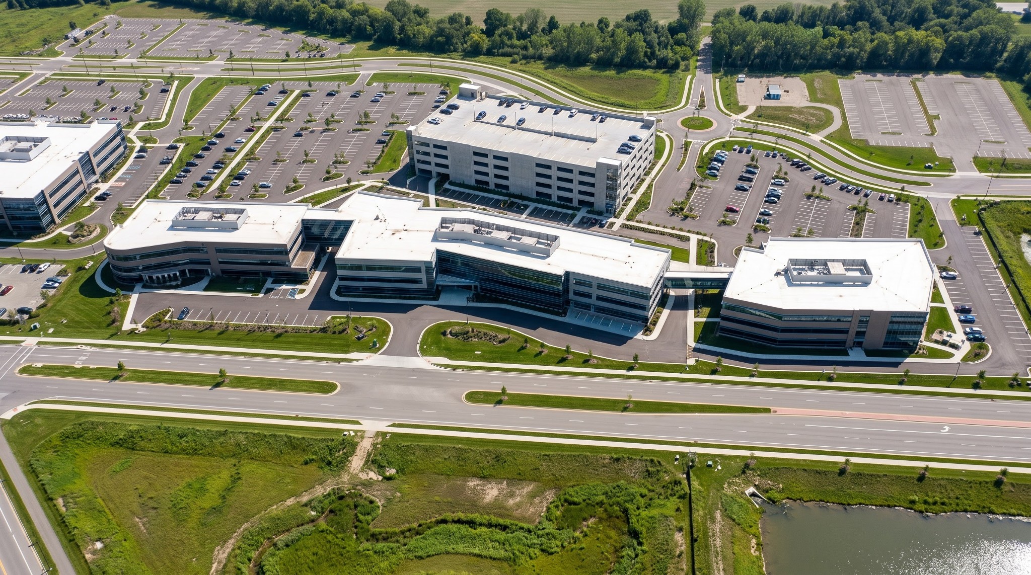 Oblique aerial drone photograph of the proposed NetJets corporate headquarters campus expansion at 4111 Bridgeway Avenue, showing the parking garage, office buildings BW1 through BW4, surface parking, and detention basins.