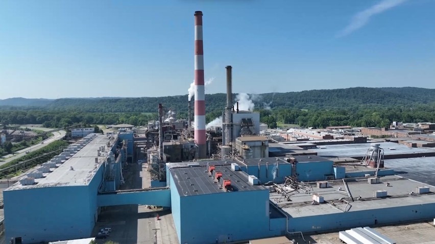 High-angle drone view of the Chillicothe paper mill showing blue production buildings and smokestacks backed by wooded hills.
