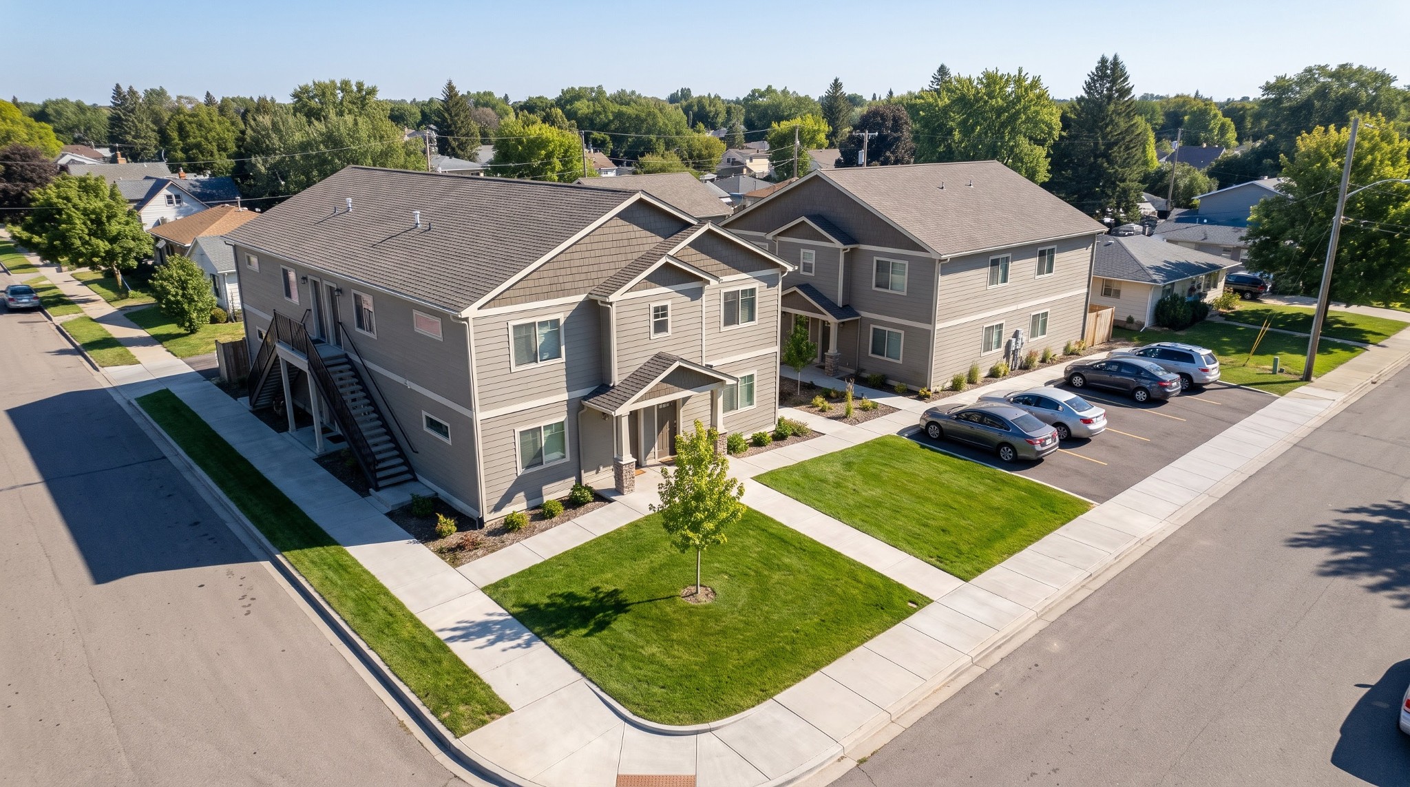Illustrative aerial rendering of two two-storey residential buildings on a corner lot with pitched roofs, exterior stairs, and rear parking.