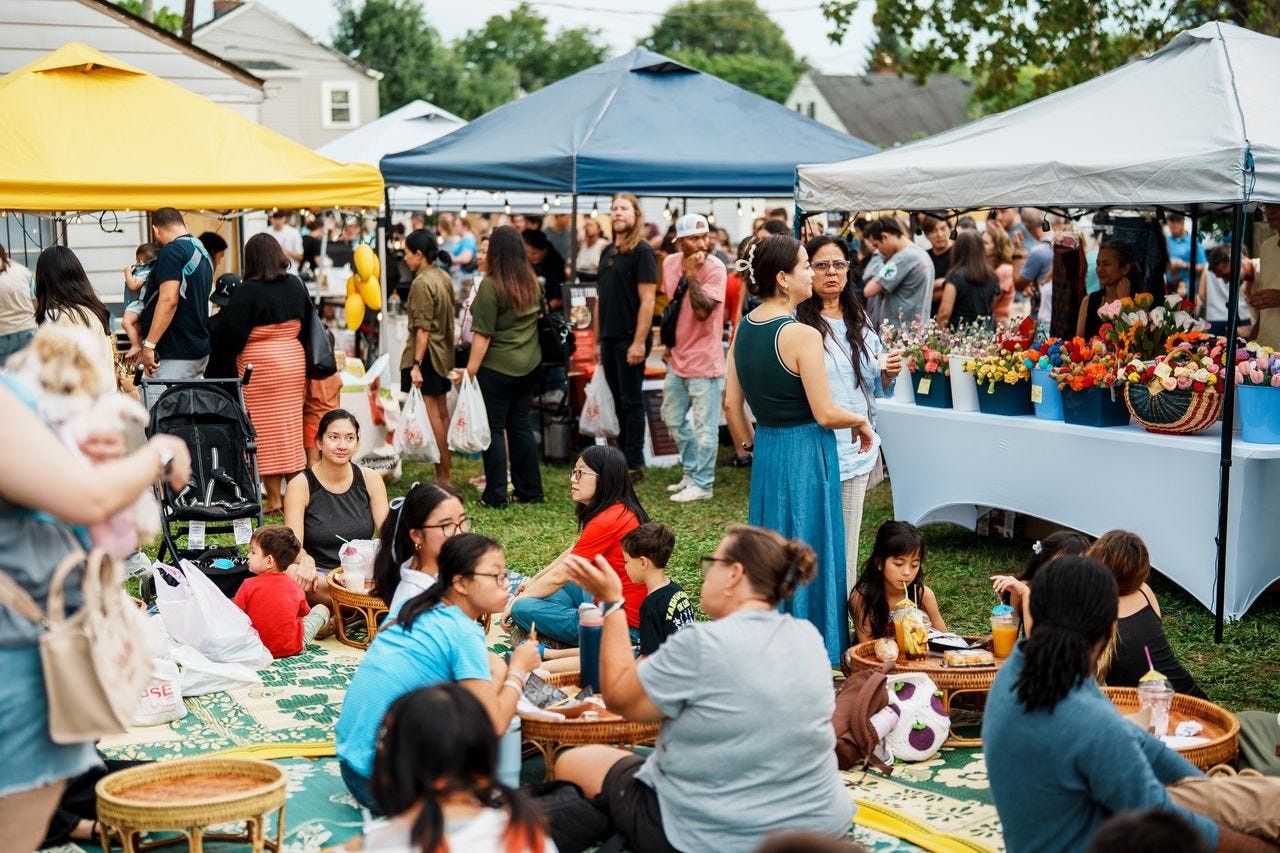 Crowds gather on a grassy lawn with pop-up vendor tents and food stalls at an outdoor Asian market in Columbus.