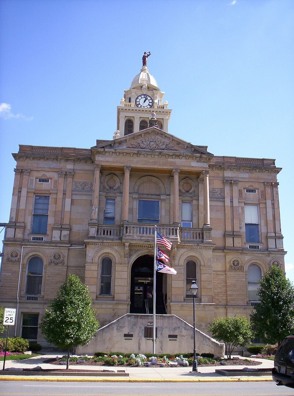 Exterior view of the historic stone Marion County Courthouse in Marion, Ohio, featuring arched windows, flags, and a clock tower topped by Lady Justice.