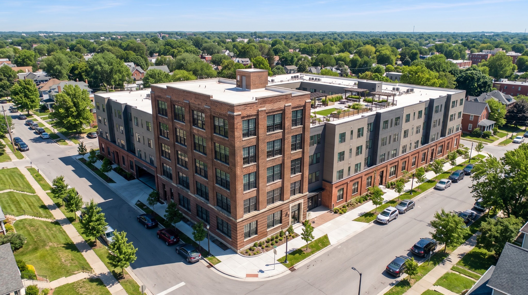 Aerial view of a renovated six-story red brick industrial tower and an attached four-story contemporary apartment building with a rooftop terrace.