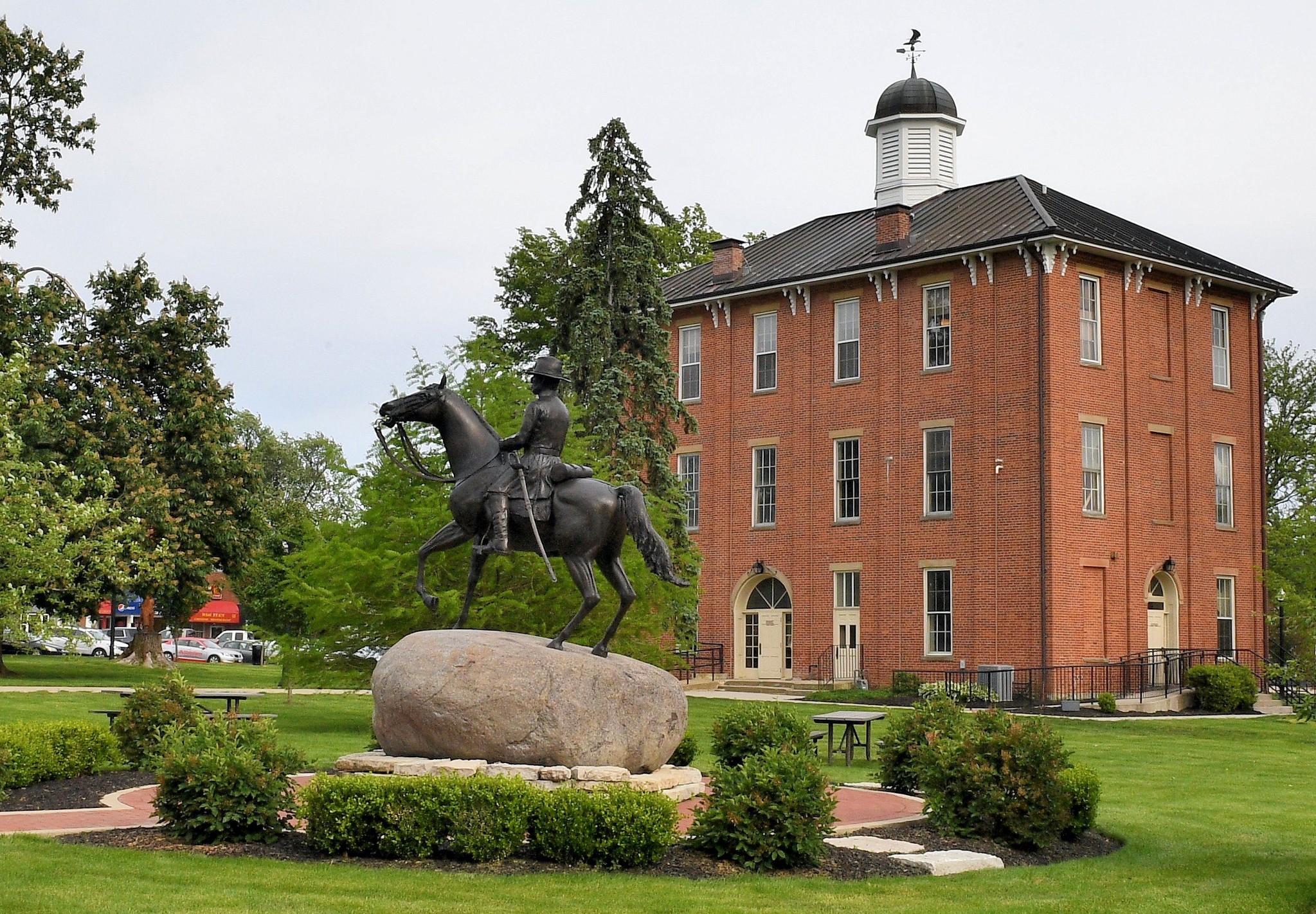Sunbury Town Hall, a historic three-story red-brick building with an octagonal cupola, behind an equestrian statue on a boulder in Sunbury, Ohio.