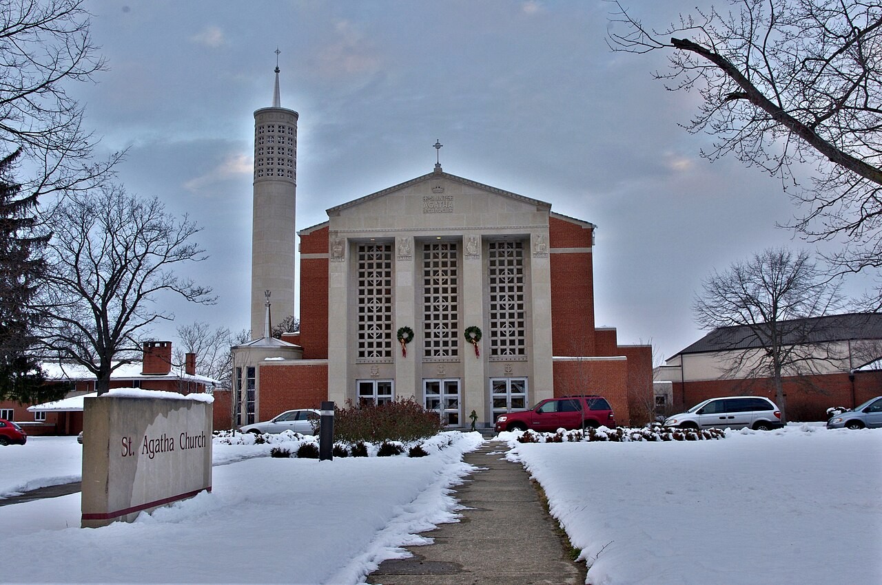 Exterior winter view of Saint Agatha Catholic Church in Upper Arlington with snow covering the lawn, a brick bell tower, and a front sign.