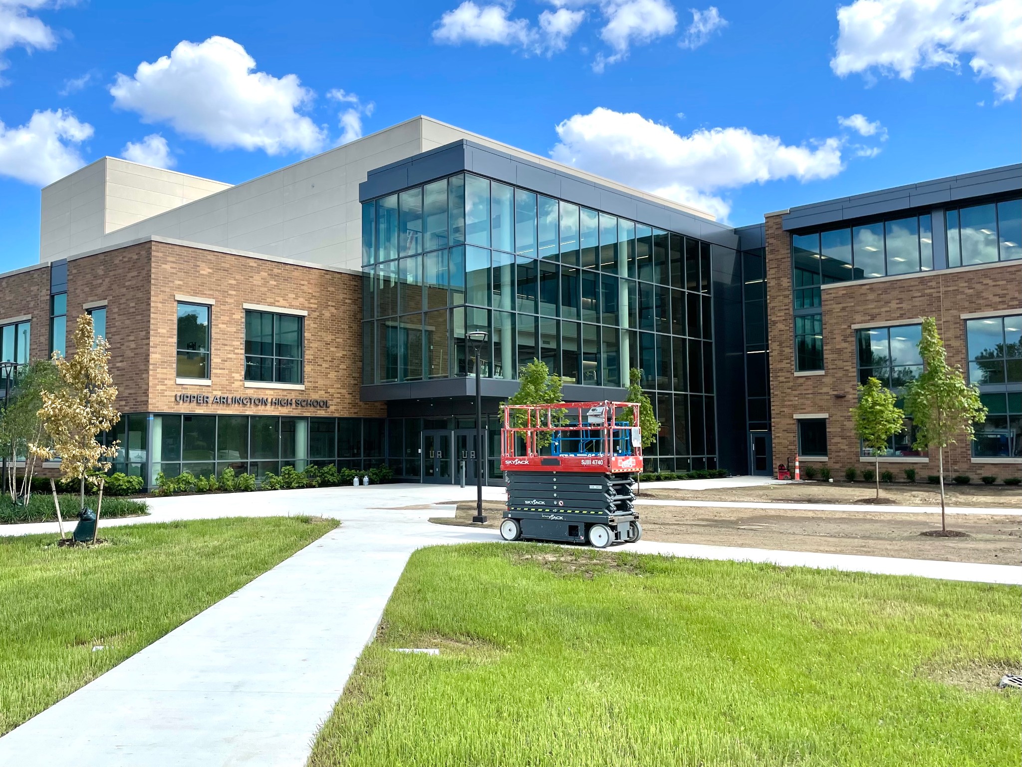 Exterior facade of Upper Arlington High School with brick and glass windows, concrete plaza, and green lawn.