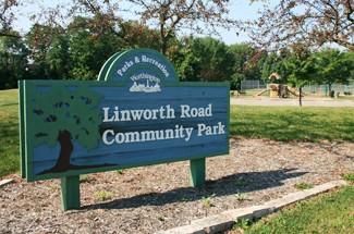 Linworth Road Community Park wooden entrance sign with park grounds, playground, and tennis courts in the background.