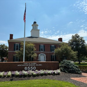 Exterior of the red brick Louis J.R. Goorey Worthington Municipal Building with a central white cupola, flagpole, and civic entrance sign.
