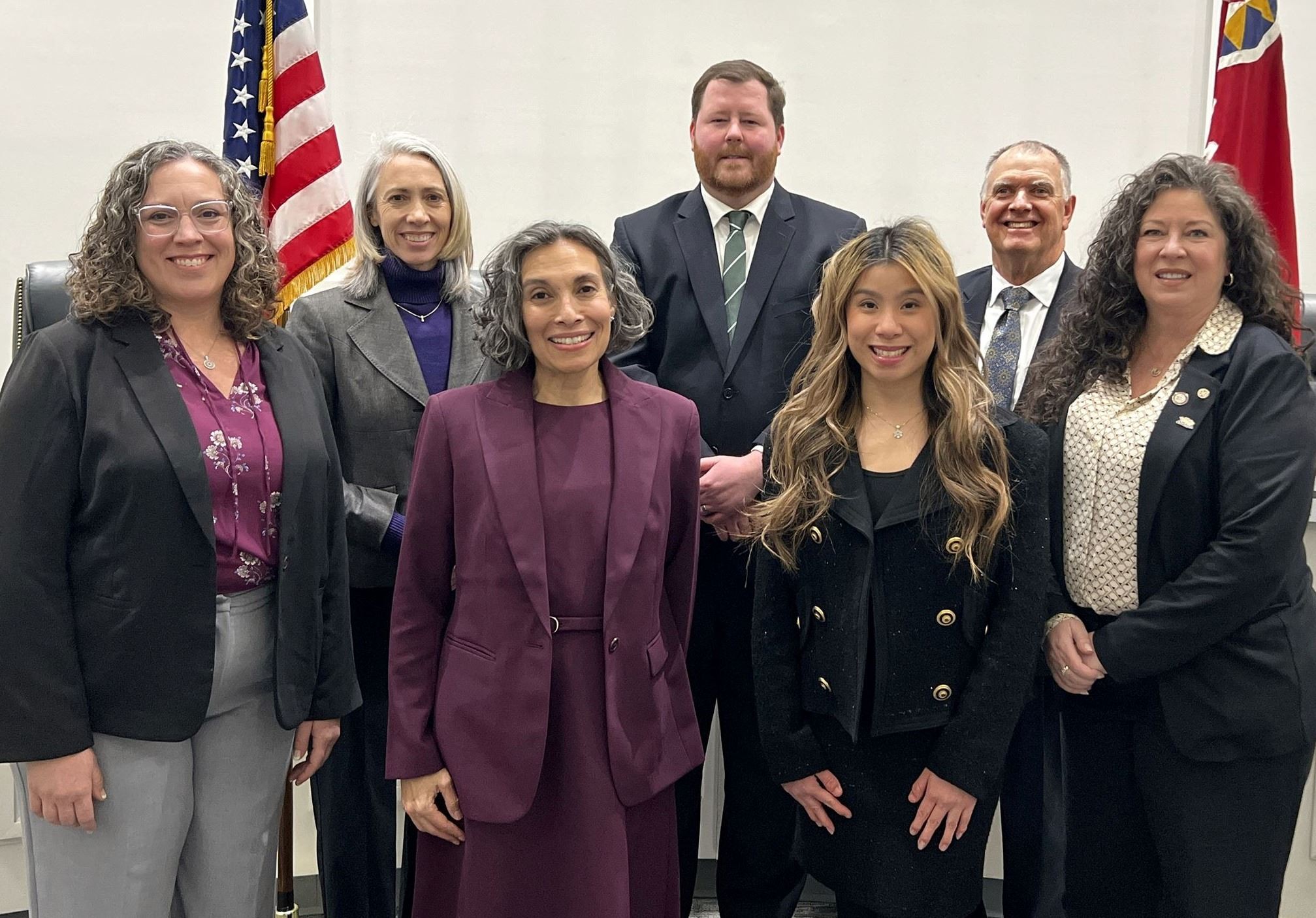 Seven members of the Worthington City Council standing together in professional business attire flanked by the United States and municipal flags.